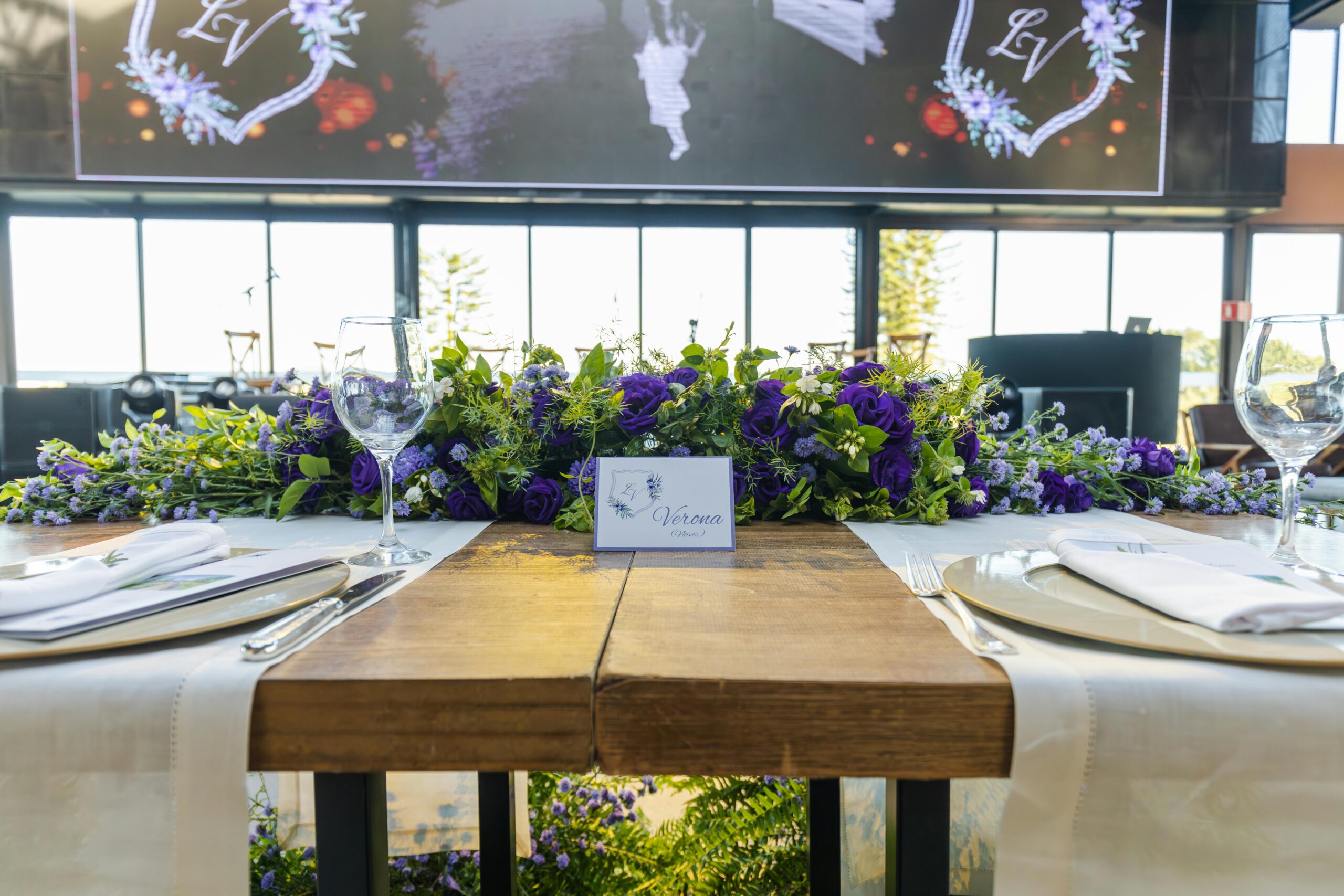 Beautiful wedding table featuring a vibrant purple and green floral arrangement, elegant place settings, and wineglasses.